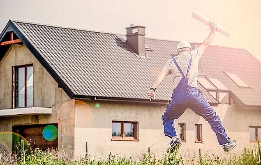 Ein fröhlicher Bauherr springt vor seinem Haus in die Luft